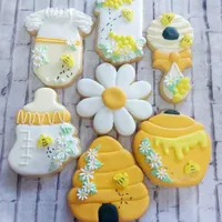 Adorable bee-themed baby shower iced cookies with honey pots, bees, daisies, and baby onesies