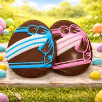 Large 12cm chocolate Easter eggs decorated with blue and pink icing on wooden board with colorful Easter eggs in spring grass
